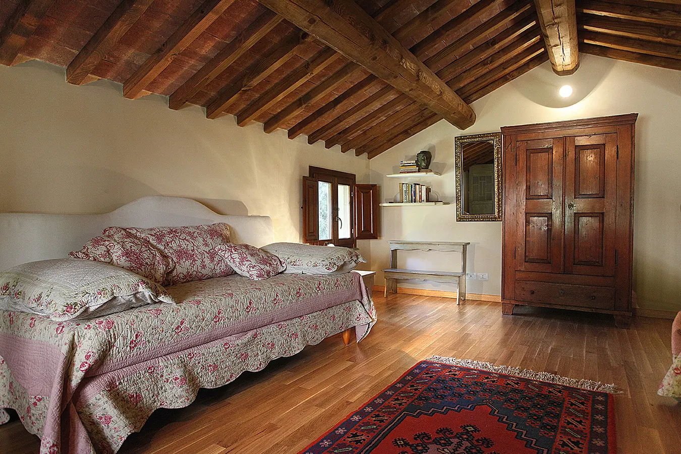Camera da letto rustica con letto matrimoniale, armadio in legno e soffitto con travi a vista