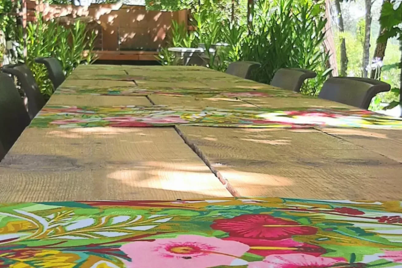 Tavolo all’aperto con tovaglia floreale e sedie intorno, in un giardino ombreggiato
