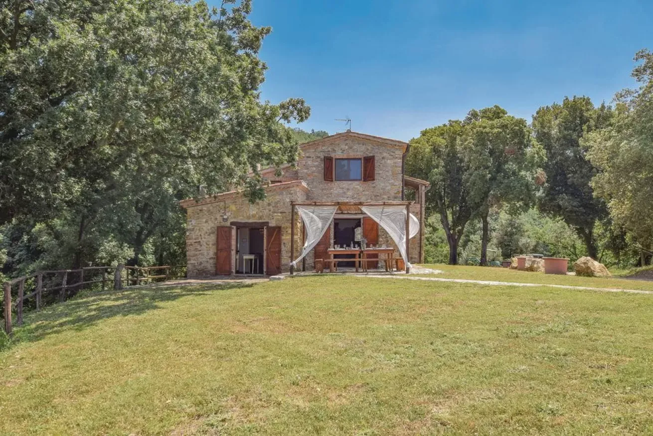 Stone house with a covered patio in a grassy clearing surrounded by trees