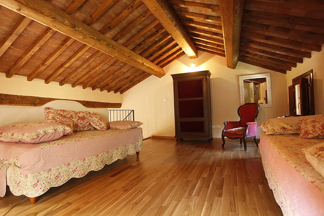 Camera da letto rustica con travi in legno a vista, due letti singoli e poltrona rossa
