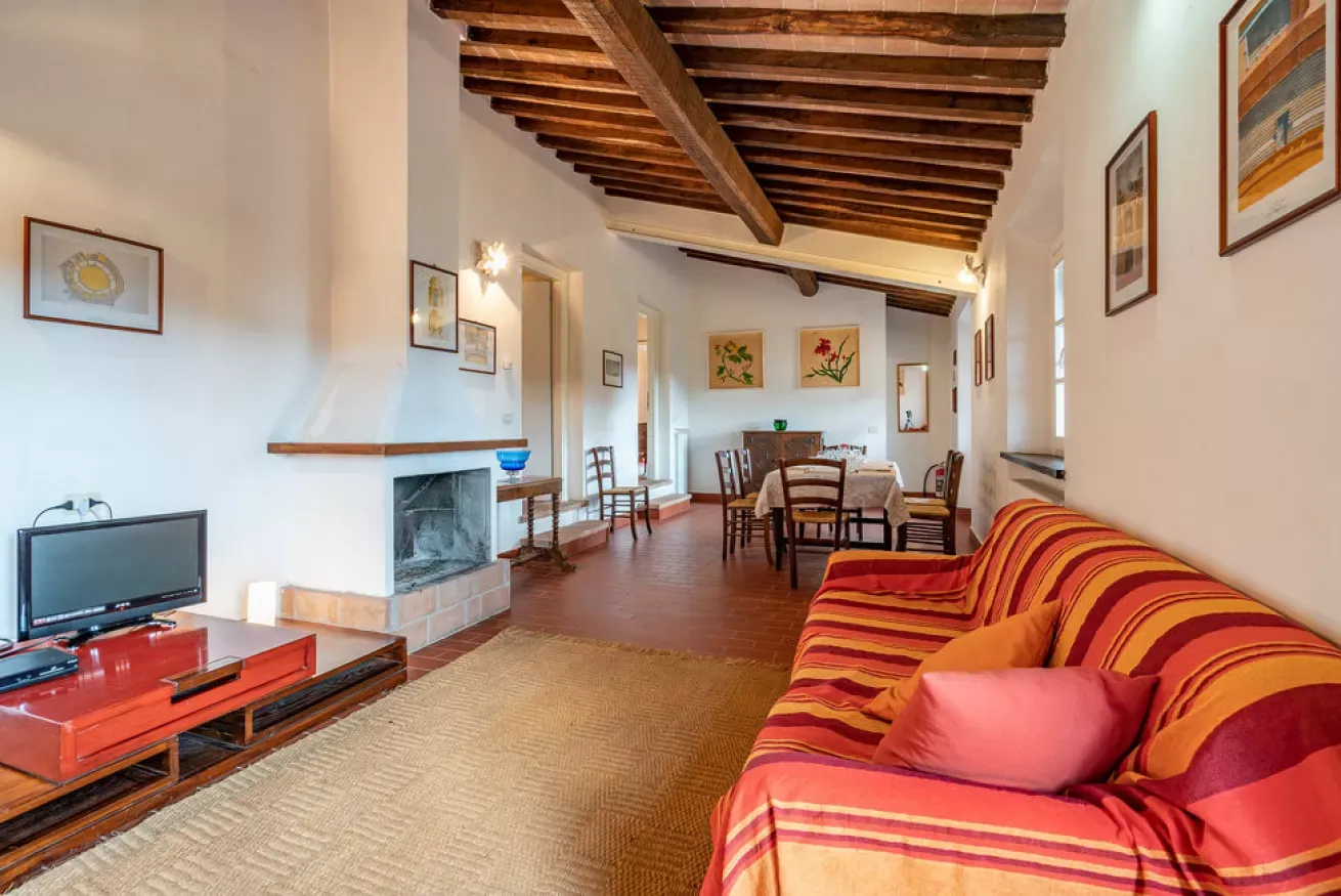 A rustic living room with exposed wooden beams, a striped sofa, fireplace, TV, and dining table