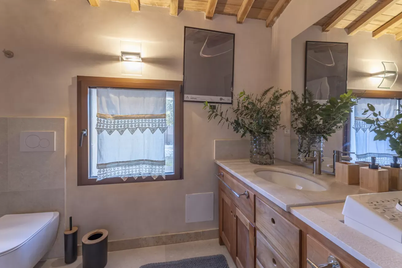 Bagno con lavabo in legno, specchio grande, finestra con tenda e piante decorative