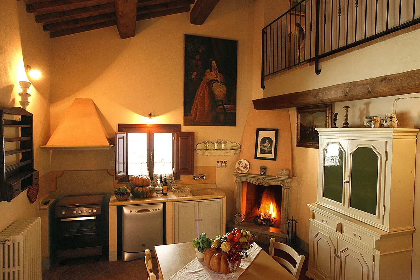 Cucina rustica con camino acceso, tavolo apparecchiato e mobili bianchi in legno