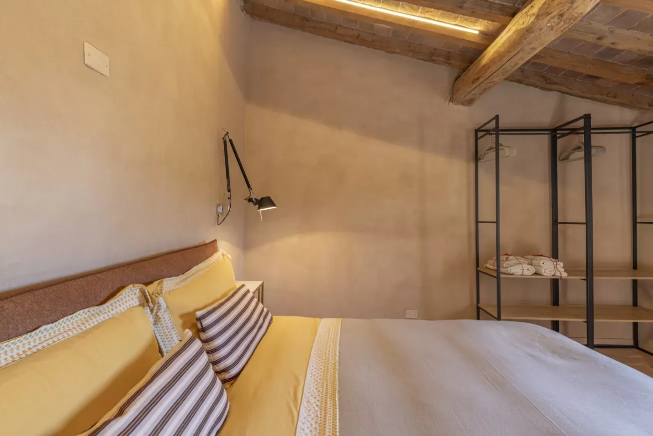 Camera da letto con letto matrimoniale, lampada da parete e armadio aperto con asciugamani e grucce