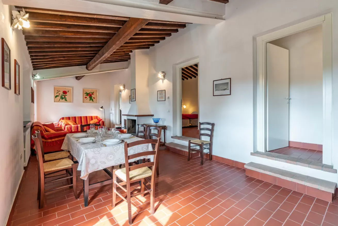 Dining room with a set table, chairs, and a sofa in a rustic interior with exposed wooden beams