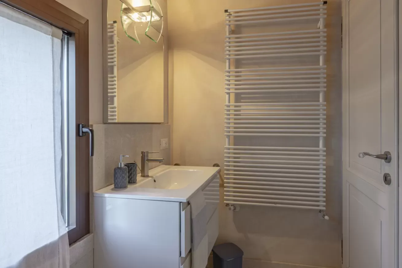 Bagno con lavabo, specchio, finestra e termoarredo bianco