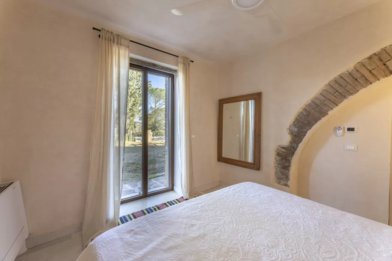 Camera da letto luminosa con letto, finestra a tutta altezza e parete in pietra a vista