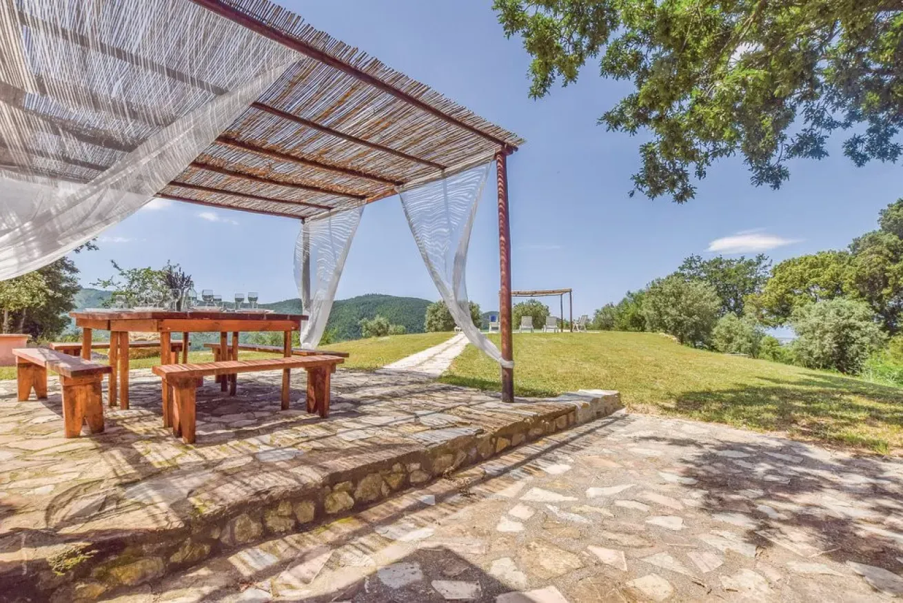 Outdoor picnic area with wooden tables under a shaded pergola overlooking a grassy hillside