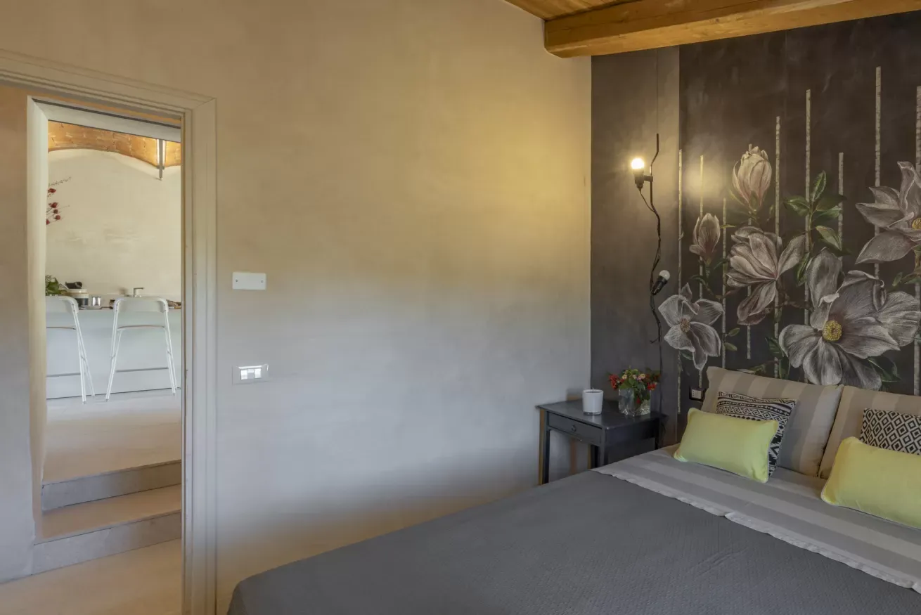 Camera da letto con letto matrimoniale, parete decorata con fiori e porta aperta verso la cucina