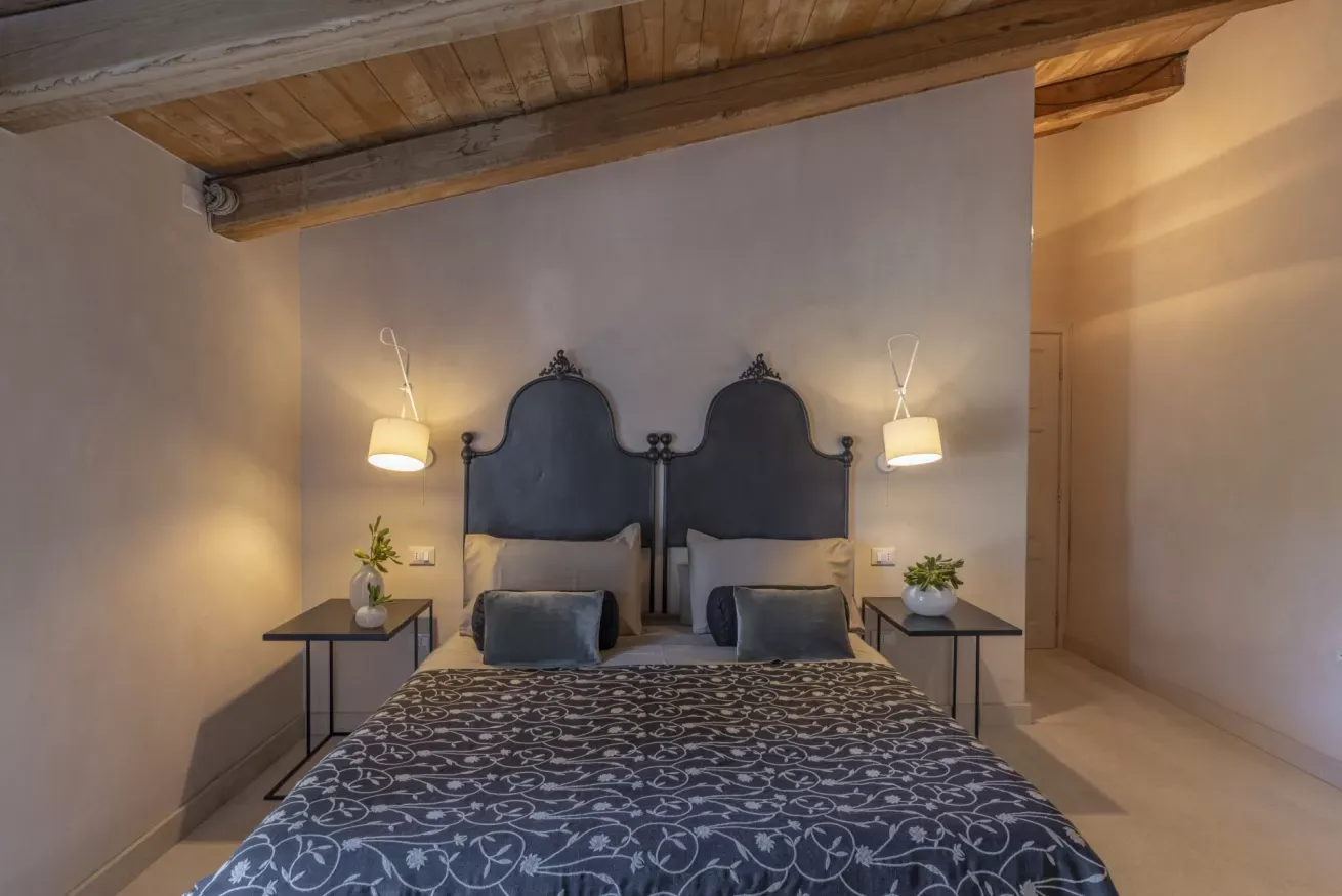 Camera da letto con letto matrimoniale, testiere alte, comodini e lampade da parete sotto un soffitto con travi in legno