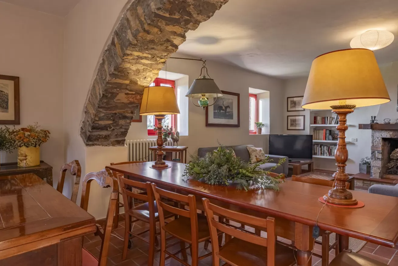 Rustic dining room with a long wooden table, lamps, and a stone archway