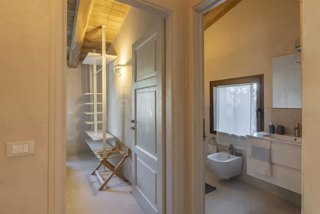 Interno con due bagni visibili, uno con lavabo e specchio, l’altro con scaffalature e sedia pieghevole
