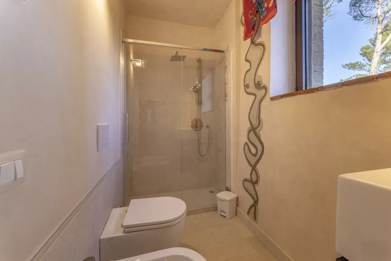 Bagno con doccia in vetro, WC e finestra aperta sul verde