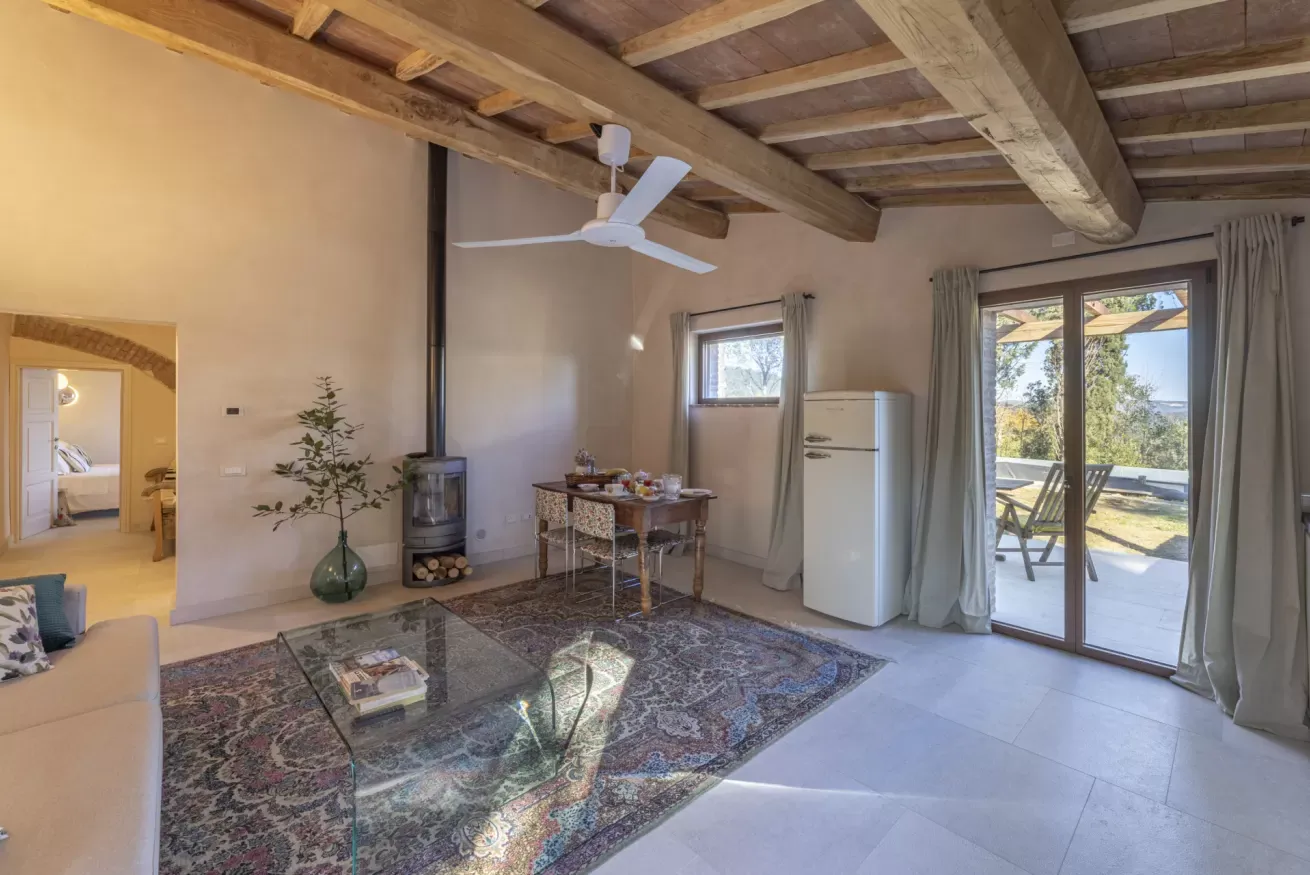 Soggiorno luminoso con travi a vista, stufa a legna, tavolo da pranzo e porta finestra sul patio