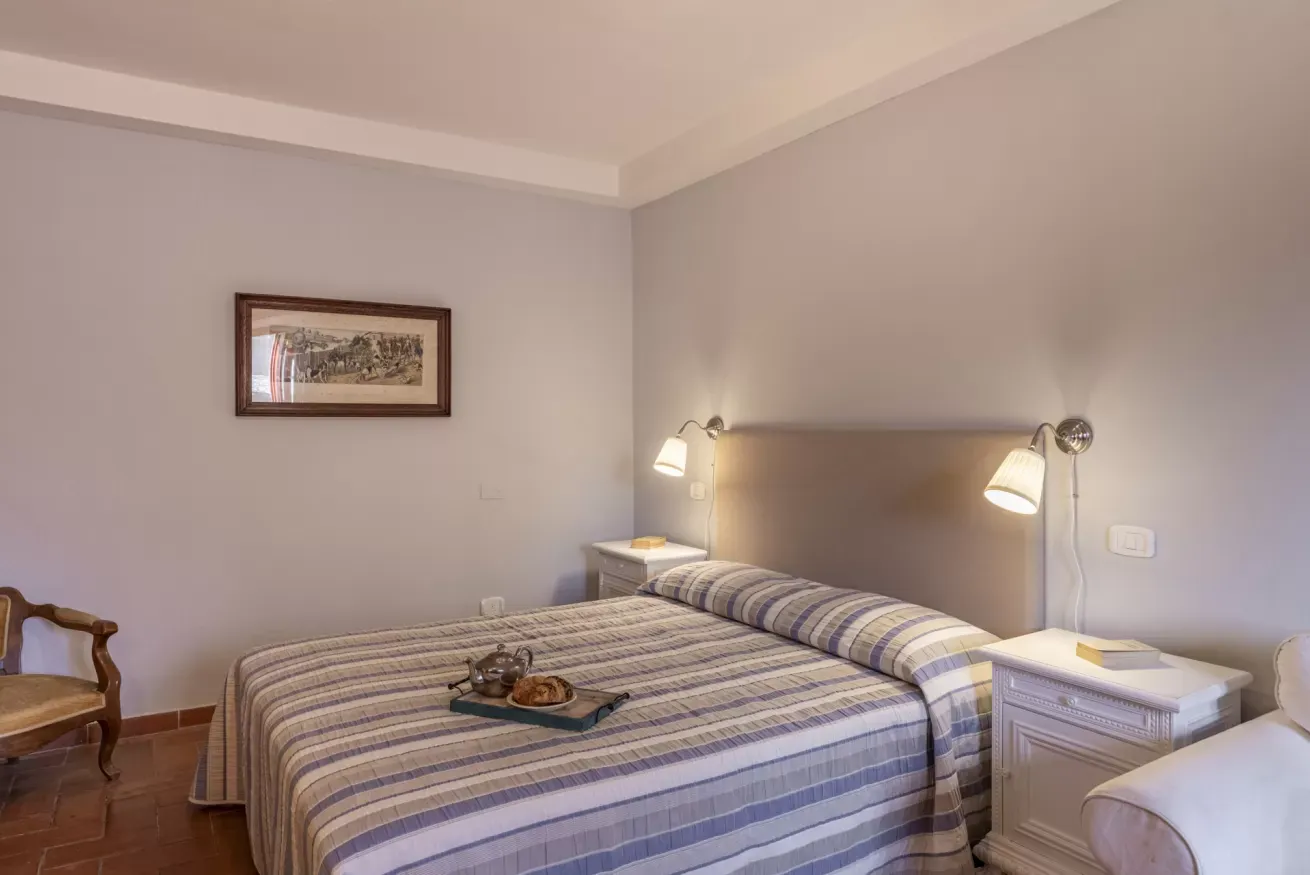 A neatly made bed in a softly lit bedroom with bedside lamps and a framed picture on the wall