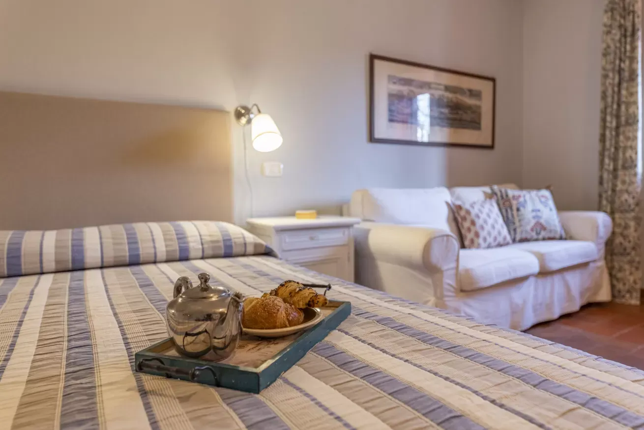 Bedroom with a tray of tea and pastries on the bed, beside a sofa and bedside lamp