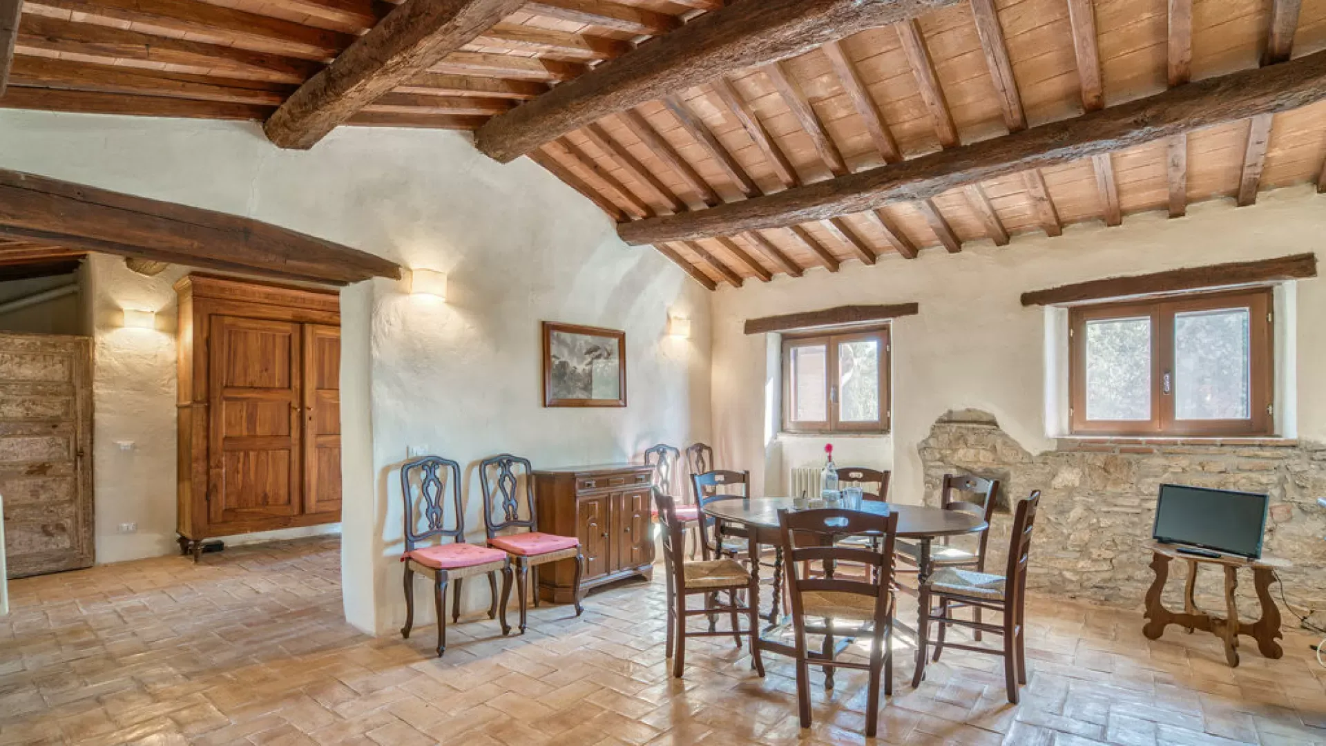 Rustic dining room with exposed wooden beams, stone walls, a round table, and chairs