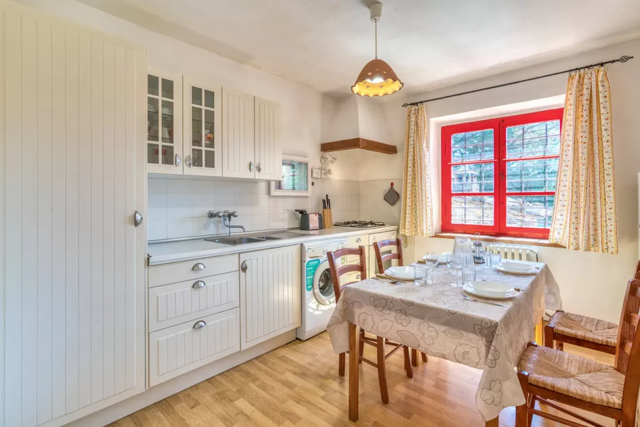 Bright kitchen with white cabinets, a dining table, and a red-framed window