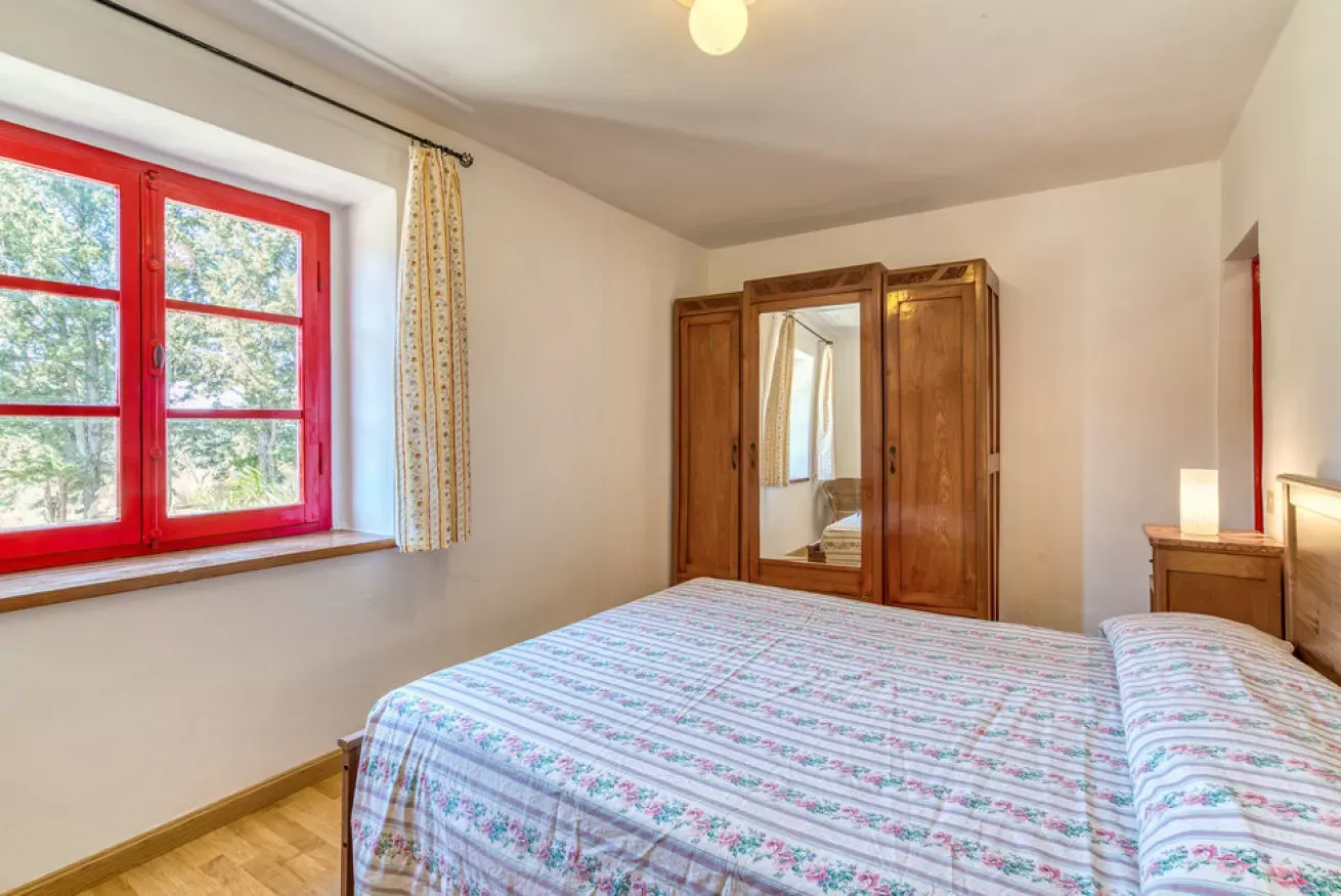 Bedroom with red-framed window, wooden wardrobe, and bed with floral bedspread